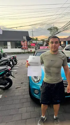A customer holding the rental agreement in front of a blue car